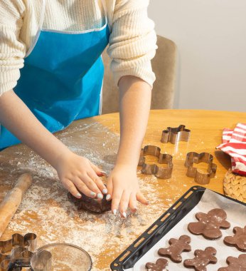 Çocuk ellerine yakın çekim. Mutfak masasında un ve keskiyle kurabiye hamuru hazırlıyorlar. Aile yemekleri, kaynaşma ve yaratıcılık kavramı parlak doğal ışıkta