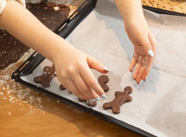 Çocuklar, ebeveynler ve çocuklar evde kurabiye pişiriyorlar. Un kaplı masada kurabiye keskisi kullanarak çikolata hamuru yuvarlamak. Ev yapımı pastalar ve tatil aile aktiviteleri.