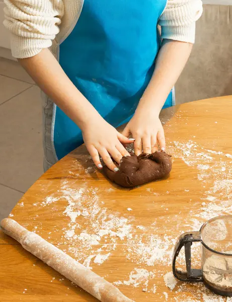 Çocuk ellerine yakın çekim. Mutfak masasında un ve keskiyle kurabiye hamuru hazırlıyorlar. Aile yemekleri, kaynaşma ve yaratıcılık kavramı parlak doğal ışıkta