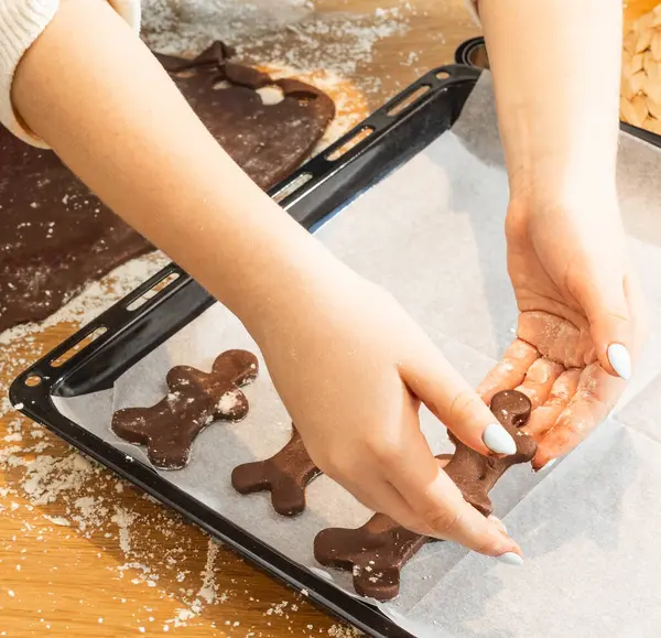 Çocuklar, ebeveynler ve çocuklar evde kurabiye pişiriyorlar. Un kaplı masada kurabiye keskisi kullanarak çikolata hamuru yuvarlamak. Ev yapımı pastalar ve tatil aile aktiviteleri.