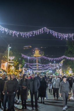 HAIFA, ISRAEL 23 ARALIK 2024: İnsanlar Noel ve Hanuka ışıklarıyla süslenmiş Ben Gurion Bulvarı boyunca yürür, arka planda Bah Gardens