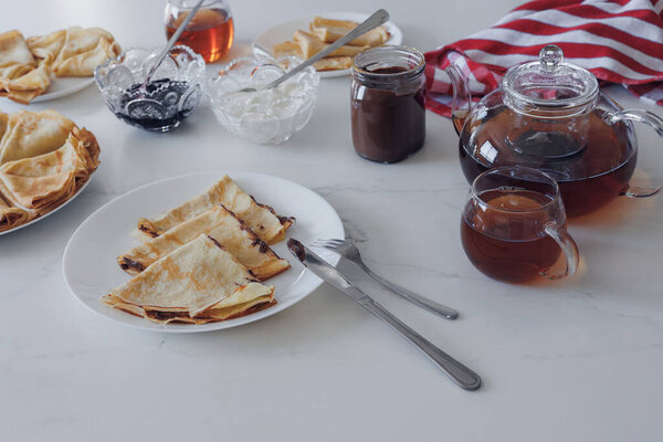 Traditional crepes with jam, sour cream and tea served on white table. Top view, cozy homemade atmosphere and culinary concept