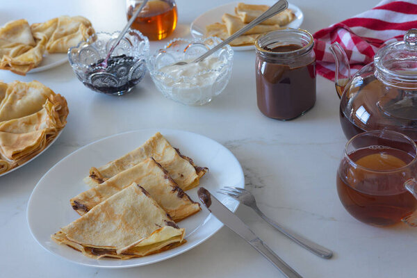 Traditional crepes with jam, sour cream and tea served on white table. Top view, cozy homemade atmosphere and culinary concept