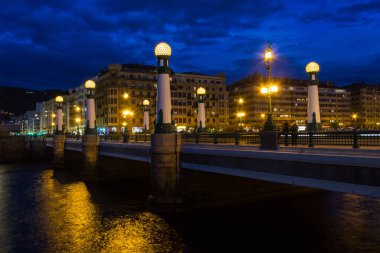 Historic Zurriola Bridge over Urumea river under dark blue sky at twilight in the city of San Sebastian, Spain. Transportation concept, urban landscape at night concepts