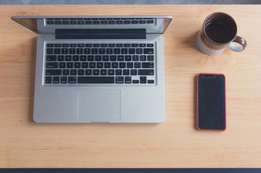 Grey laptop open next to coffee mug and cell phone from top. Home desktop. Ready to start working concept. Vintage effect