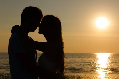Couple of lovers silhouette passionately close to each other at sunset celebrating Valentines Day by the sea in the island of Koh Phangan, Thailand. Romantic scene, passionate lovers on the beach