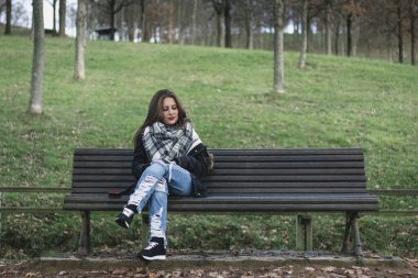 Young woman sitting on park bench looking down to space next to her. Missing someone, heart broken concepts