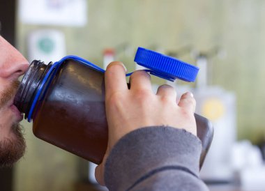 Young man with beard and mustache drinking from plastic sports bottle with blue lid