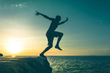 Man jumping over a cliff into the sea on sunset in Koh Phangan island, Thailand. Vintage effect. Dare, fearless concept. Two out of three series.