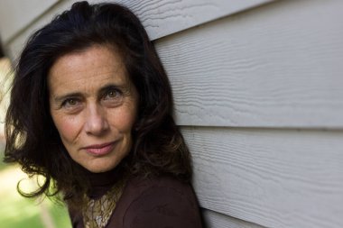 Açık havada beyaz tahta duvara yaslanan zarif, olgun bir kadının yoğun bakışları. Güzel orta yaşlı bayan gülümsemesi