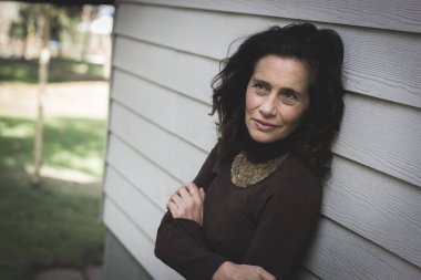 Göğsünde çapraz kollar olan düşünceli olgun bir kadın beyaz tahta duvara yaslanıyor. Endişeli bakışları olan orta yaşlı bir kadın. Sorunlar, endişeler, üzüntü, depresyon kavramları