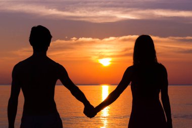 Romantic Valentine's Day scene of a young couple silhouettes holding hands by the sea staring at colorful sunset in the island of Koh Phangan, Thailand. Honeymoon destination, love concept