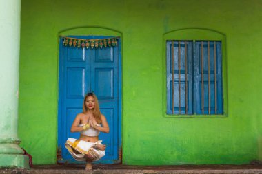 Indian yoga teacher in half bound lotus tiptoe pose. Female yogi with traditional Kerala white sari by blue door on green wall. Young woman with hands in anjali mudra. Focus, balance concepts