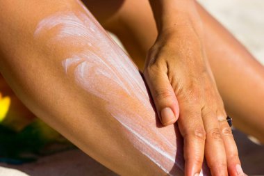 Close up on woman's upper arm and hand spreading sun cream at the beach on a hot, sunny day. Tanning, sunblock spread, skin care, ultraviolet rays protection, cancer prevention concept