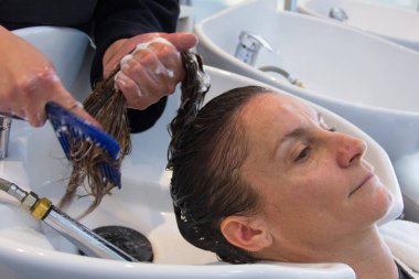 Young woman getting head washed and hairdresser trying to untangle hair with comb. Female customer at beauty salon