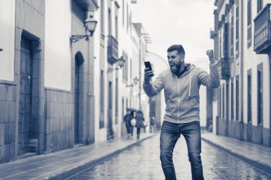 Elinde yumruğu olan şanslı genç adam şehrin yağmurlu sokaklarında cep telefonuyla zaferini kutluyor. Tam sakallı hippi modeli, gri kapüşonlu ve öforik ifadeli. Satır bahsi kazananı, neşeli konsept