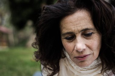 Parktaki orta yaşlı güzel kadının hüzünlü portresi. Endişeli ve depresif ifadeli olgun bir kadın. Kötü haber, melankolik, karamsar konsept