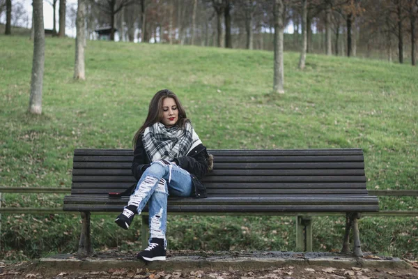 Young woman sitting on park bench looking down to space next to her. Missing someone, heart broken concepts