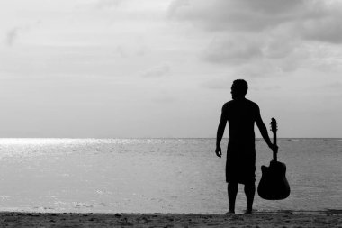 Gitarını tutan genç adamın silueti gün batımında Tayland 'ın Koh Phangan adasında denize bakarken. Müzik sanatçısı ilham buluyor. Siyah beyaz fotoğraf.