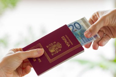 İçinde 20 Euro 'luk banknot olan İspanyol pasaportu tutan bir kadının eli ve onu almak üzere olan bir adamın eli. Rüşvet, ayrıcalık, itaat kavramı. Çeviri: Avrupa Birliği, İspanya, pasaport