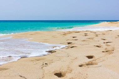 Deniz kıyısında turkuaz suyla birlikte ayak izleri. Tropikal adanın renkli denizinde kimse yok. Idyllic yaz tatilleri konsepti