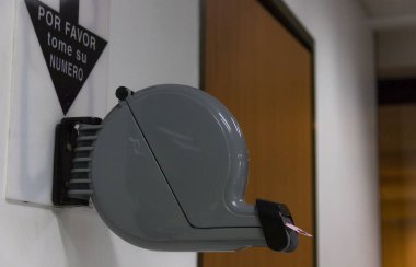 Klinik resepsiyon odasında bir numaralı bilet makinesi. İspanyolca çeviri: Lütfen bir numara alın. Bürokrasi, idari ofis, sıraya girin, konsept bekleyin.