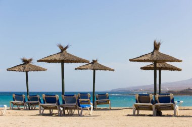 Fuerteventura 'daki boş plajda mavi hamaklı hasır güneş şemsiyeleri. Caleta de Fuste, Kanarya Adaları 'nda güneşli bir günde kimse yok. Yaz tatilleri, turizm krizi kavramları