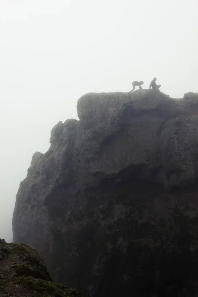 Inexperienced climbers struggle to move forward on top of mountain rock in Roque Nublo, Gran Canaria. Silhouette of couple trying to climb down on dense foggy day. Trouble concept