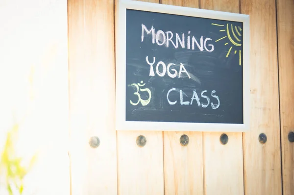 Morning yoga class board sign hanging from wood door on sunny day. Om symbol