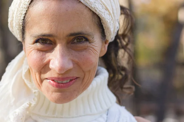 stock image Close up on confident mature woman smiling with white turtle neck knitted sweater and shawl on head. Happy middle aged lady portrait. Autumn fashion sales, hippie style, skin care concepts