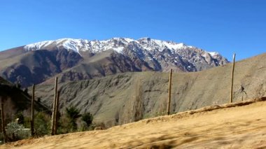 Sırt çantalı iki genç sarışın kız, Elqui Vadisi 'nde, güzel güneşli bir günde, arka planda Andes dağları olan Şili' nin arka planında kirli bir patikadan geçiyorlar.