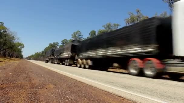 アウトバックオーストラリアの空の道路を通過する3つのトレーラーを持つ大型トラック 砂漠の高速道路の木々に囲まれた 長距離貨物輸送 運転者の職業概念 — ストック動画