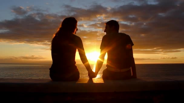 海のそばに座っている男女は グラン カナリアのメロネラス ビーチウォークで日没を楽しむ カップルシルエットカラフルな夕暮れを見つめキスを開始します バレンタインデー 新婚旅行のロマンチックなデートの概念 — ストック動画