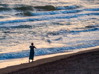 Gün batımında sahilde yürüyen bir kadın. 