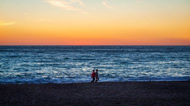 İnsanlar gün batımı sırasında sahilde