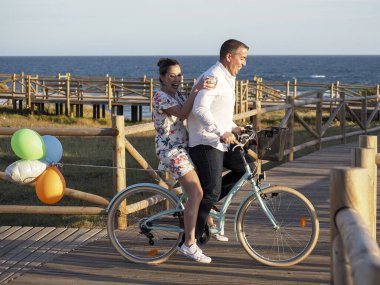 Genç mutlu çift sahilde yürüyor ve bisikletleriyle romantik vakit geçiriyorlar..