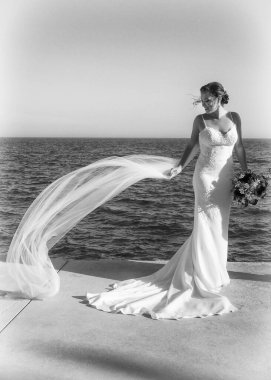Güzel gelin denizin önünde elbisesini giyiyor.