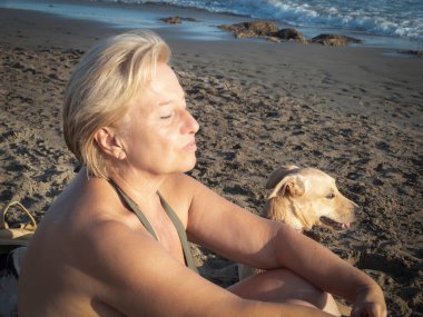 Gün batımında sahilde köpekli yaşlı bir kadın.