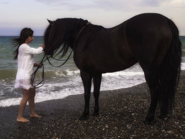 Sahilde atın yanında duran bir kadın.