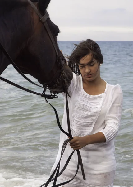 Beyaz elbiseli bir kadın atın yanında duruyor.