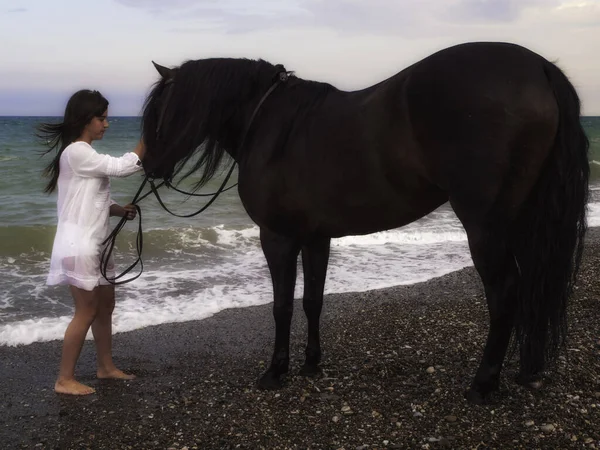 Sahilde atın yanında duran bir kadın.