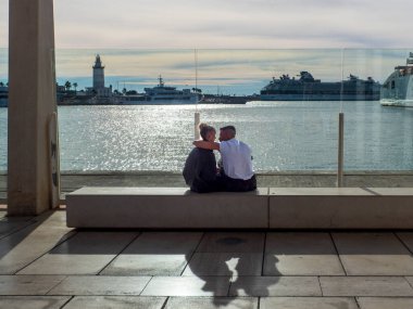 Malaga, Spain.  12/07/2024.  A bride and groom sitting on the edge of pier one of the port of the Andalusian city of Malaga. clipart