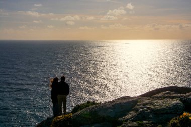 Galiçya sahilindeki Finisterre Burnu 'nda gün batımını bekleyen çift..