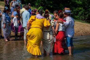 Huelva, Endülüs, İspanya. 4 Haziran 2025. Geleneksel Endülüs dalgalı elbiseler giymiş kadınlar geleneksel El Roco Bakiresi onuruna yapılan geleneksel kutsal yolculukta Quema Nehri 'nin karşı kıyısına geçerler..