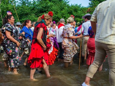 Huelva, Endülüs, İspanya. 4 Haziran 2025. Geleneksel Endülüs dalgalı elbiseler giymiş kadınlar geleneksel El Rocio Bakiresi onuruna yapılan geleneksel kutsal yolculukta Quema Nehri 'nin karşı kıyısına geçerler..