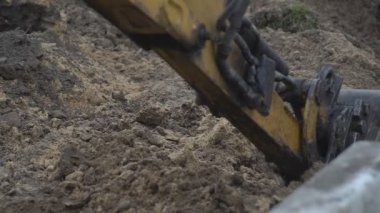 Kazıcı inşaat alanında faaliyet gösteriyor. Stok görüntüleri. Kazıcının alt görüntüsü mavi bulutlu arkaplanda kumla dolu sarı renkli kovayı ters çeviriyor.