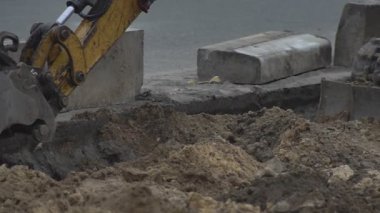 Kazıcı inşaat alanında faaliyet gösteriyor. Stok görüntüleri. Kazıcının alt görüntüsü mavi bulutlu arkaplanda kumla dolu sarı renkli kovayı ters çeviriyor.