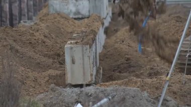 Kazıcı inşaat alanında faaliyet gösteriyor. Stok görüntüleri. Kazıcının alt görüntüsü mavi bulutlu arkaplanda kumla dolu sarı renkli kovayı ters çeviriyor.