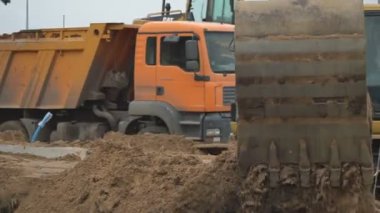 Kazıcı inşaat alanında faaliyet gösteriyor. Stok görüntüleri. Kazıcının alt görüntüsü mavi bulutlu arkaplanda kumla dolu sarı renkli kovayı ters çeviriyor.