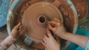 Çocuklar için çömlekçilik yüksek lisansı. Çömlekçilerin çarkında dönen yarım kalmış seramik vazonun ve profesyonel aletlerle kil şekillendiren ellerin yakın çekimi. Eathenware ve geleneksel çömlek konsepti yaratmak.